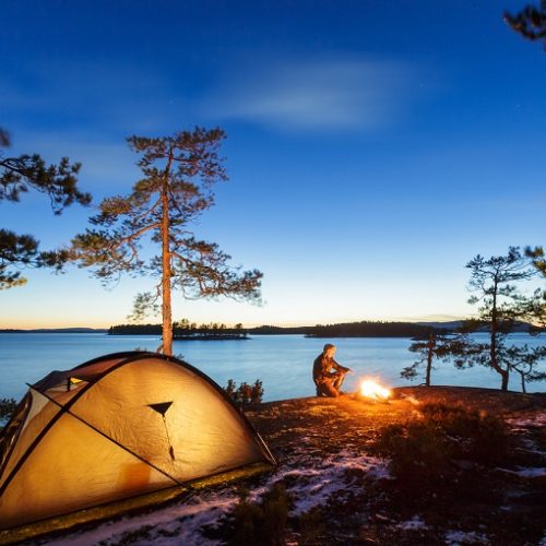 Man is sitting around a campfire and just relaxing, snow on the ground